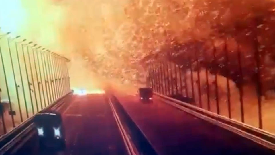 Two vehicles drive across Kerch Strait Bridge as it becomes engulfed in flames and smoke after an explosion.