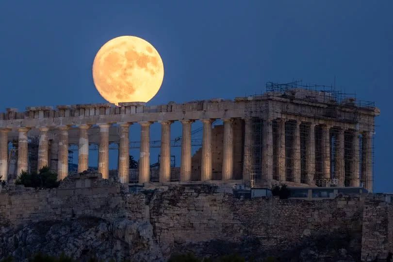 The moon rises in the sky behind the Parthenon temple at the ancient Acropolis hill in Athens