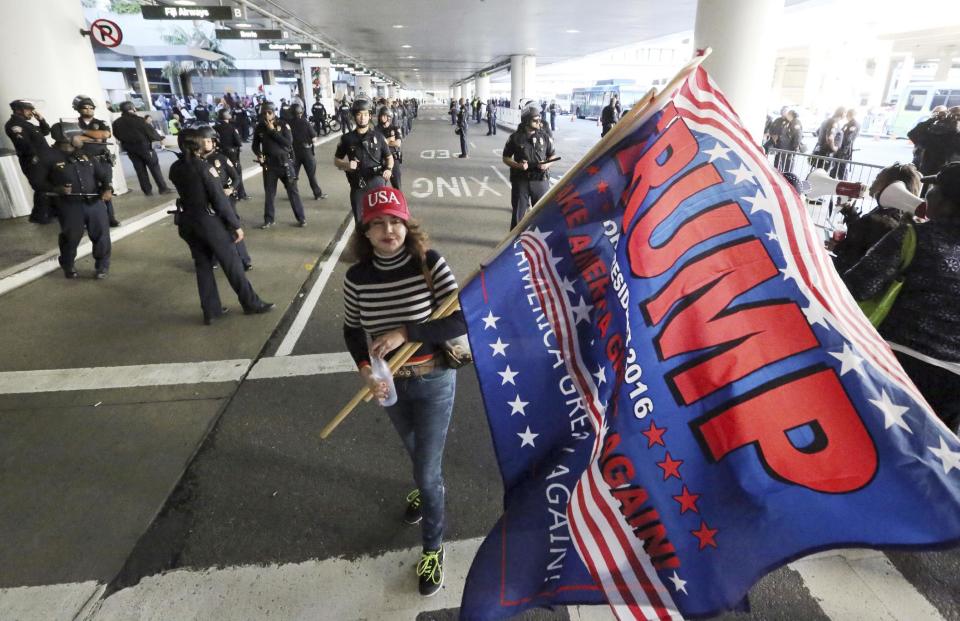 A woman who supports President Donald Trump's executive order barring entry to the U.S. by seven Muslim-majority countries waves a Trump campaign flag in front of a police skirmish line, meant to keep pro- and anti-Trump protesters apart, at the Tom Bradley International Terminal at Los Angeles International Airport on Saturday, Feb. 4, 2017. (AP Photo/Reed Saxon)