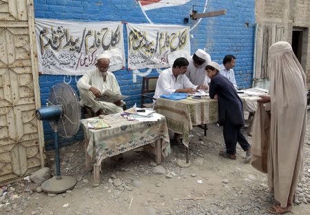 A woman watches as a boy speaks with writers filling up forms for people applying for Pakistan national ID cards in Bannu, in northwest Pakistan July 25, 2014. REUTERS/Caren Firouz