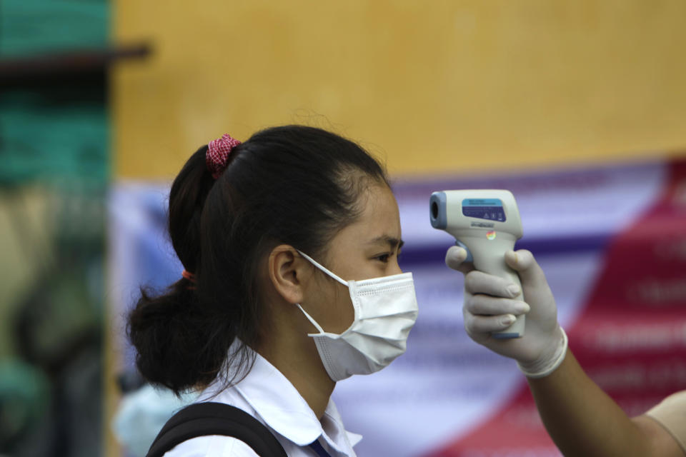 A school girl, left, has her temperature checked before she enters the Santhormok high school in Phnom Penh, Cambodia, Monday, Nov. 2, 2020. Schools throughout Cambodia that had been shut in March because of the coronavirus crisis reopened Monday, but with limits on class sizes and hours. (AP Photo/Heng Sinith)