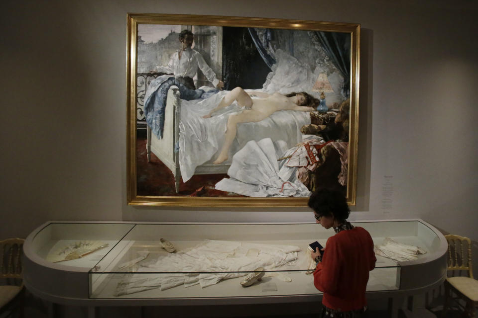 A journalist looks on women's clothing of the 19th century next to the painting of Henri Gervex, Rolla, 1878 during the press day of the Impressionism and Fashion exhibition in at the Orsay museum in Paris, Friday, Sept. 21, 2012. To coincide with Paris Fashion week, a new and highly original exhibit called "Impressionism and Fashion" opens at the Musee d'Orsay. It uses famous works of art to explore how at the dawn of impressionism, and as an emblem of "modernite" fashion, and how people dressed, became one of the main themes in art. The exhibition will open September 25, 2012 and last till January 2013. (AP Photo/Michel Euler)