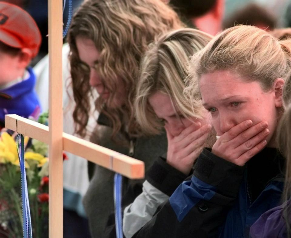 FILE - In this April 22, 1999, file photo, Columbine High School students, from left, Darcy Craig, Molly Byrne and Emily Dubin stop to pay their respects at a makeshift memorial set up in a park near the high school in Littleton, Colo. On April 20, 1999, two teenage gunmen went on a killing rampage at Columbine High School in suburban Denver. (AP Photo/Eric Gay, File)