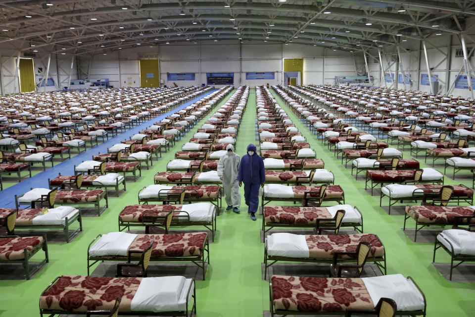 People in protective clothing walk past rows of beds at a temporary 2,000-bed hospital for COVID-19 coronavirus patients set up by the Iranian army at the international exhibition center in northern Tehran, Iran, on Thursday, March 26, 2020. (AP Photo/Ebrahim Noroozi)