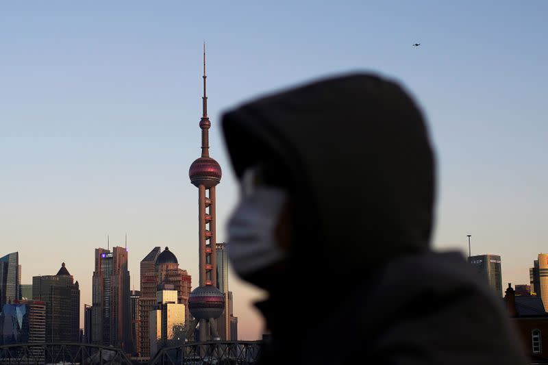 A man wearing a face mask rides a bicycle on a bridge in front of the financial district of Pudong in Shanghai