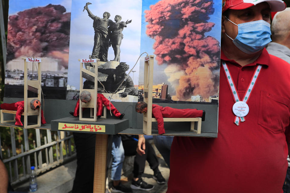 A protester holds a model of three guillotines with Arabic that reads: "The end for each of the corrupt," during a demonstration of solidarity with Judge Tarek Bitar who is investigating last year's deadly seaport blast, outside a court building in Beirut, Lebanon, Wednesday, Sept. 29, 2021. Hundreds of Lebanese, including families of the Beirut port explosion victims, rallied Wednesday outside the court of justice in support of Bitar after he was forced to suspend his work. Bitar is the second judge to take on the complicated investigation. (AP Photo/Hussein Malla)