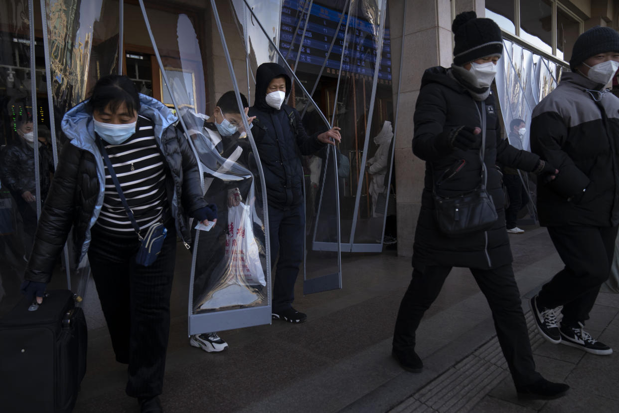 Travelers wearing face masks walk out of an exit of the Beijing Railway Station in Beijing, Saturday, Jan. 14, 2023. Millions of Chinese are expected to travel during the Lunar New Year holiday period this year. (AP Photo/Mark Schiefelbein)