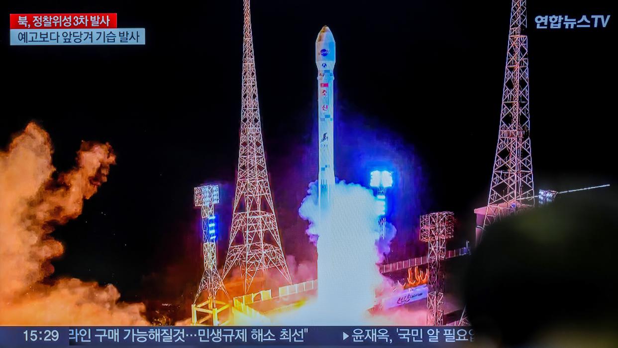  A rocket lifting off amid towers with darkness in the background. it's a tv view of the launch with Korean Hangul characters describing the scene in front. 