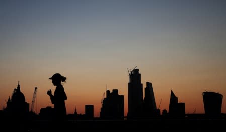 FILE PHOTO: A woman jogs as the sun rises behind the city of London financial district in London