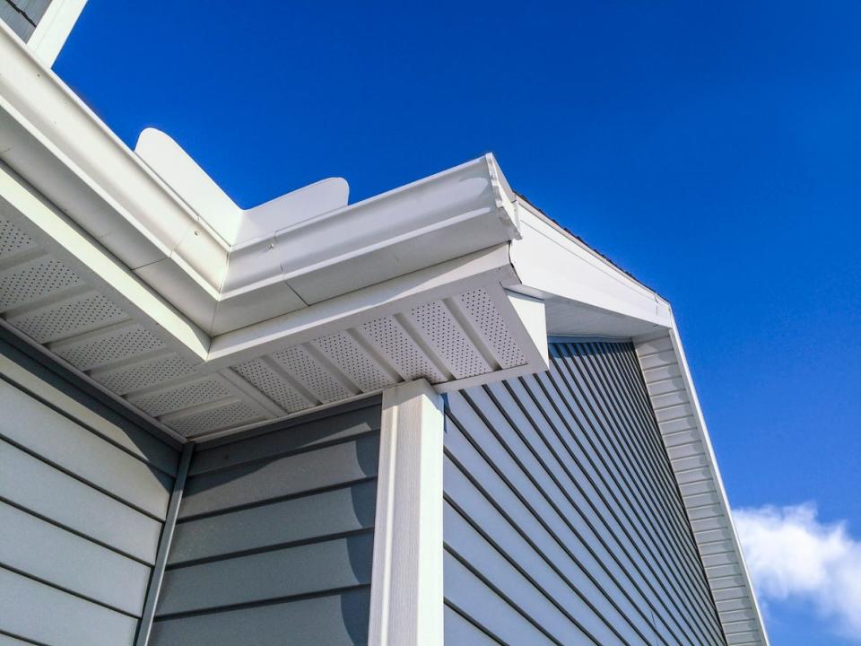 low angle view of top of house with blue vinyl siding against blue sky