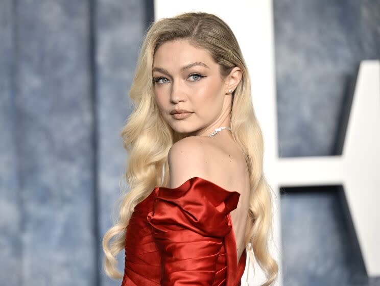 Gigi Hadid is looking over her shoulder while wearing a read strapless dress and bejeweled necklace.