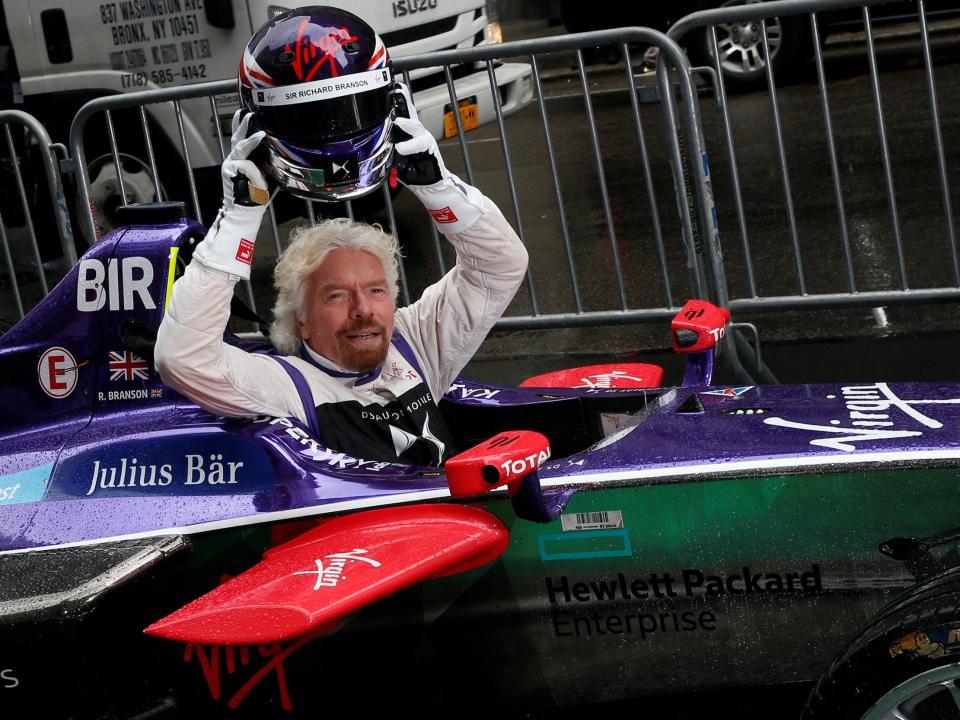 Richard Branson holds up helmet inside Formula E racecar