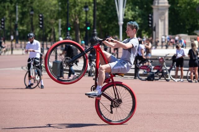 A cyclist does a wheelie outside Buckingham Palace (Dominic Lipinski/PA)