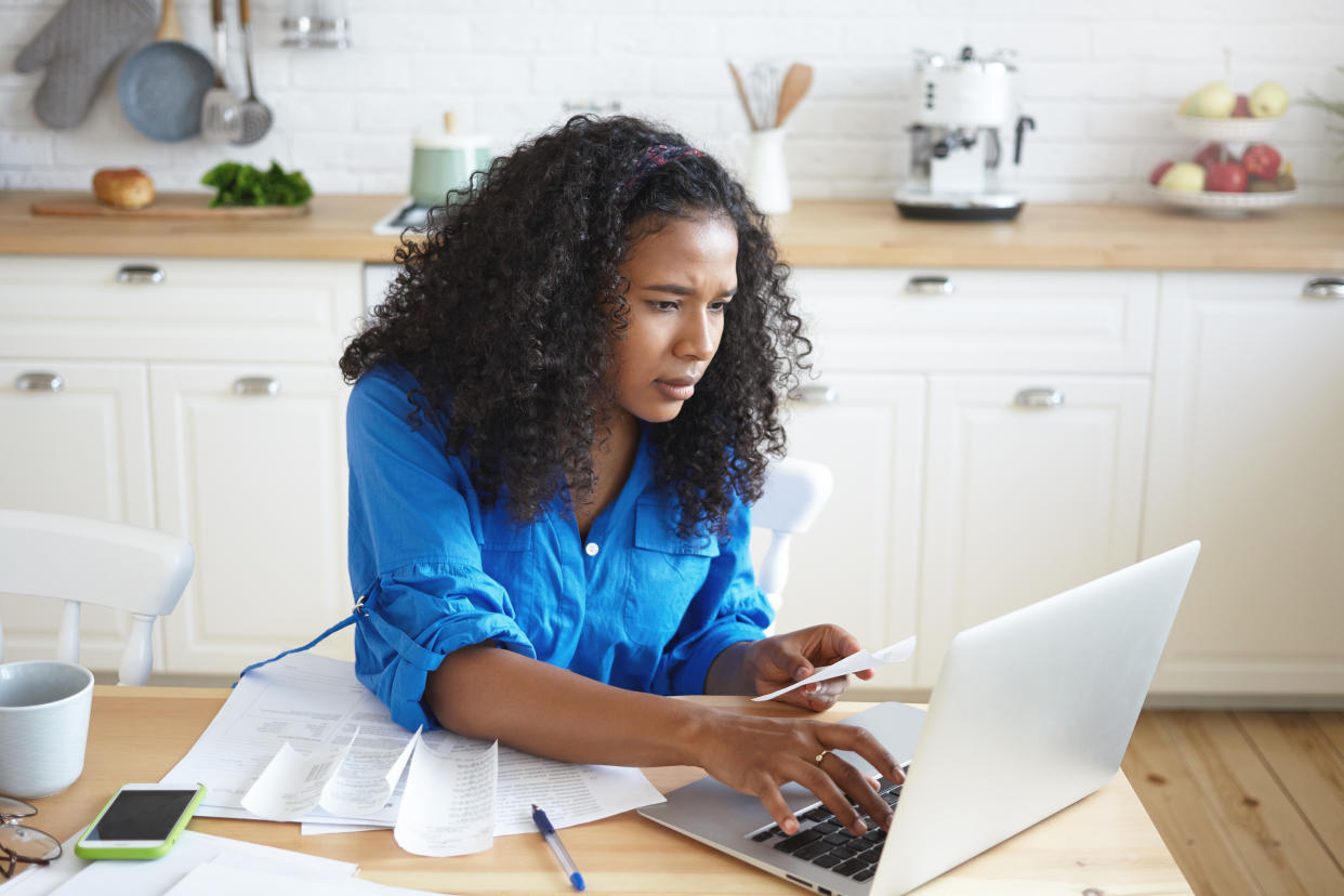 Candid shot of serious concentrated young mixed race female with curly hair typing on portable computer 