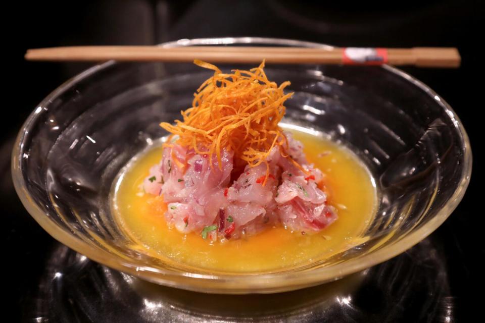 Peruvian cebiche, piled high, sits in an orange sauce in a glass bowl