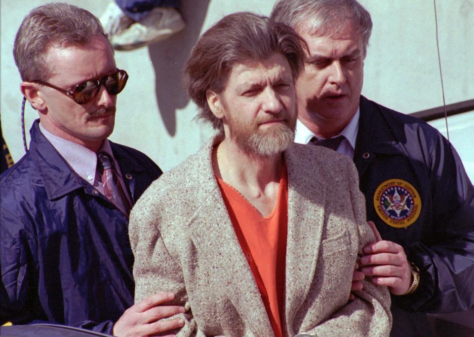 FILE — In this April 4, 1996 file photo Theodore John Kaczynski is flanked by federal agents as he is led to a car from the federal courthouse in Helena, Mont. A federal grand jury in San Francisco indicted Vladislav Victorvic Timoshchuk, on charges of mailing two envelopes containing ricin to Pelican Bay State Prison, officials announced on Friday Feb. 21, 2020. Last year the federal Bureau of Prisons intercepted a Christmas card from Timoshchuk, now living in Belarus, to Kaczynski, the convicted Unabomber, which authorizes say Timoshchuk discussed his plan to mail ricin to the United States. Kaczynski is serving a life sentence in a federal prison in Colorado for carrying out a series of mail bombings that killed three people. (AP Photo/John Youngbear, File)