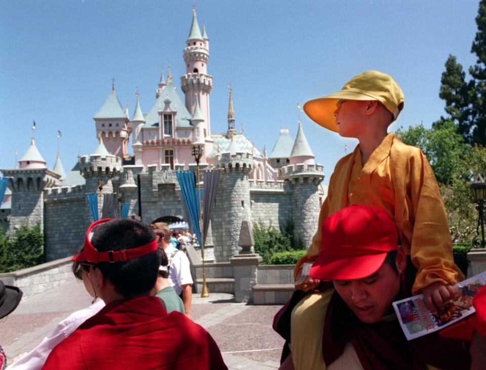 A boy in a yellow robe and hat is carried on a man's shoulders