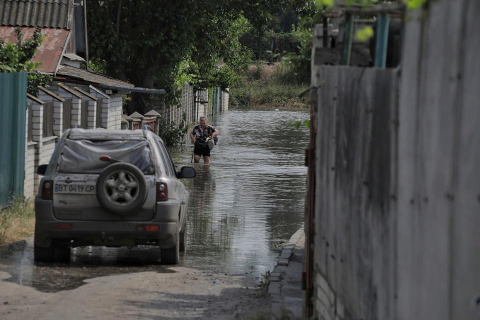 man walks through floodwaters on a street with a car parked in them