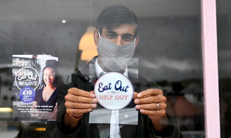 Rishi Sunak, in a face mask, putting an “Eat Out To Help Out” sticker in a window next to a small pamphlet with the same words