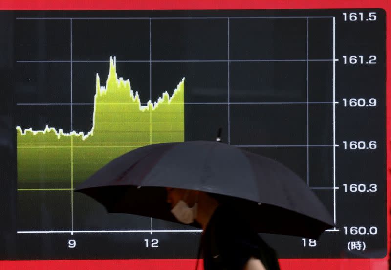 A person walks walk past an electric screen displaying the current Japanese Yen exchange rate against the U.S. dollar in Tokyo