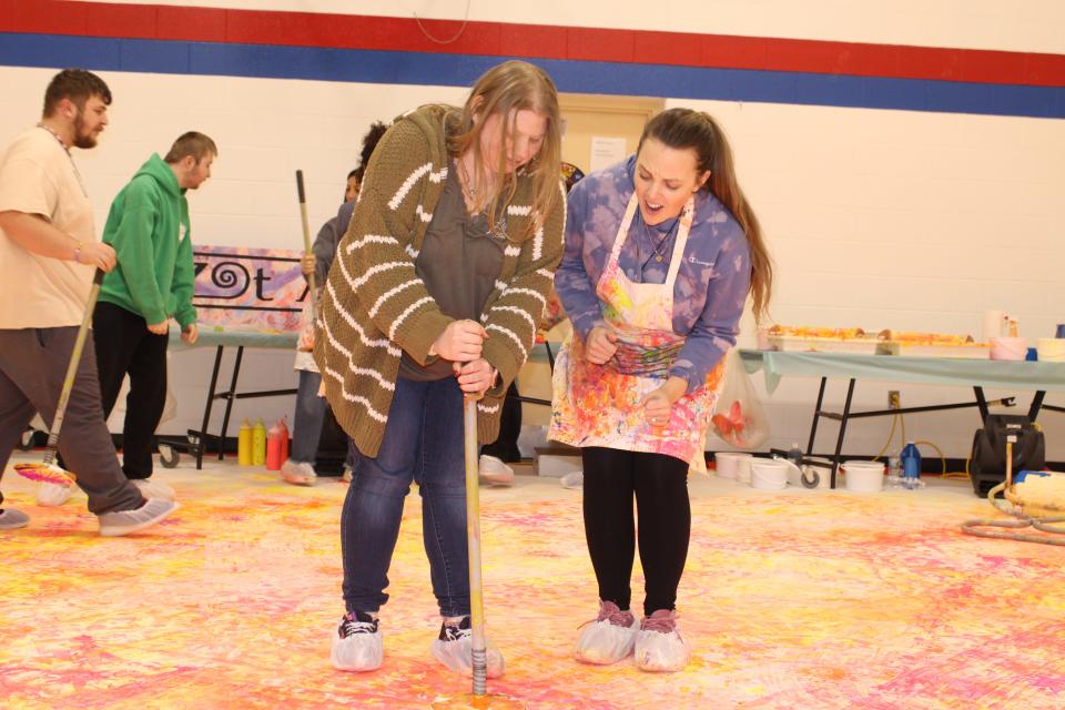 Caitlin Palm, a registered nurse at Monroe County Intermediate School District, encourages Mallory, an MCISD student, as she stamps purple images on a giant canvas.