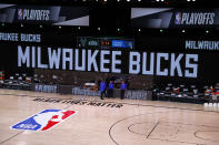 Referees stand on an empty court before the start of a scheduled game between the Milwaukee Bucks and the Orlando Magic for Game 5 of an NBA basketball first-round playoff series, Wednesday, Aug. 26, 2020, in Lake Buena Vista, Fla. (Kevin C. Cox/Pool Photo via AP)