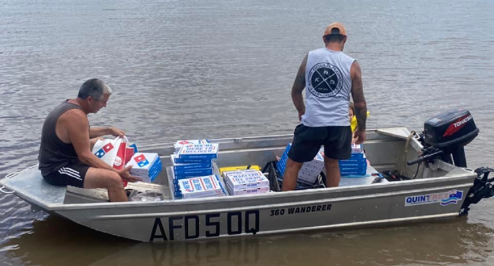 Men in a boat on floodwaters, with Domino's pizzas