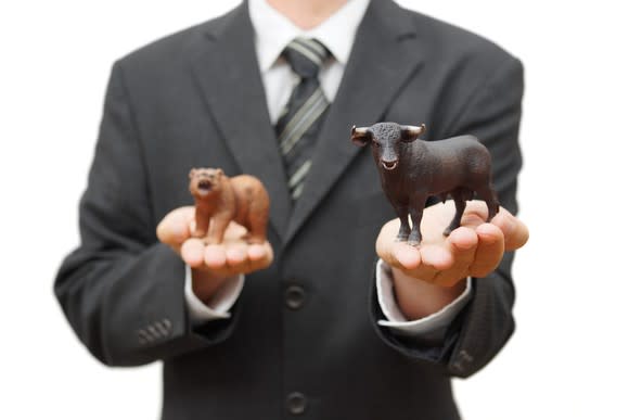 A person in a suit is holding a toy bull in one hand and a toy bear in the other.