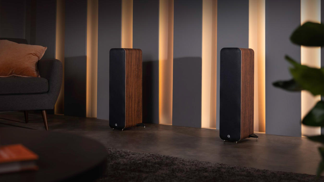  The Q Acoustics M40 speaker system in walnut positioned in a dimly lit room with grey walls and tasteful decor. 