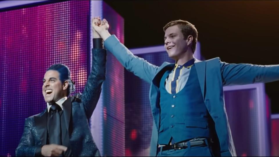 Stanley Tucci holding up Jack Quaid's hand in The Hunger Games.