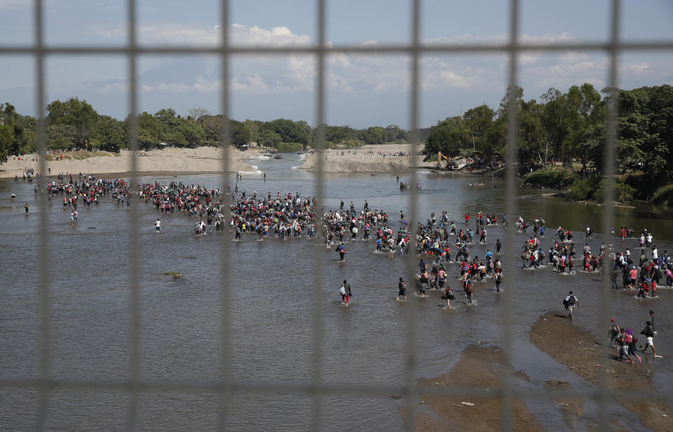 Seen through the fence on the border bridge, Central American migrants cross the Suchiate River by foot from Tecun Uman, Guatemala, to Mexico, Monday, Jan. 20, 2020. More than a thousand Central American migrants hoping to reach United States marooned in Guatemala are walking en masse across a river leading to Mexico in an attempt to convince authorities there to allow them passage through the country. (AP Photo/Moises Castillo)