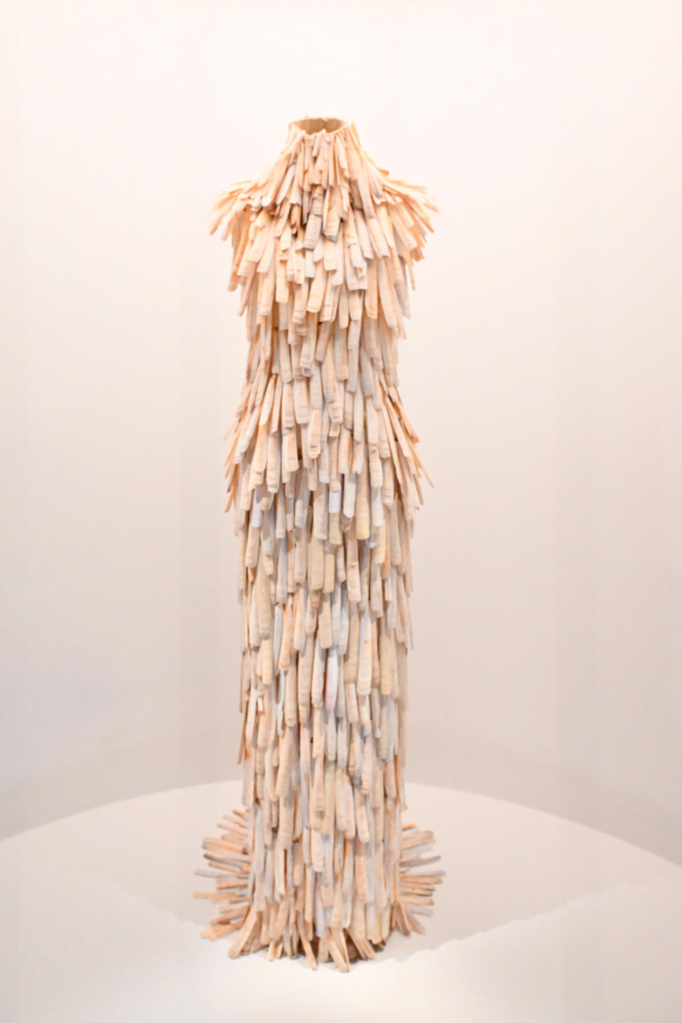 Sculptural dress made of layered material on a mannequin, displayed in a gallery setting