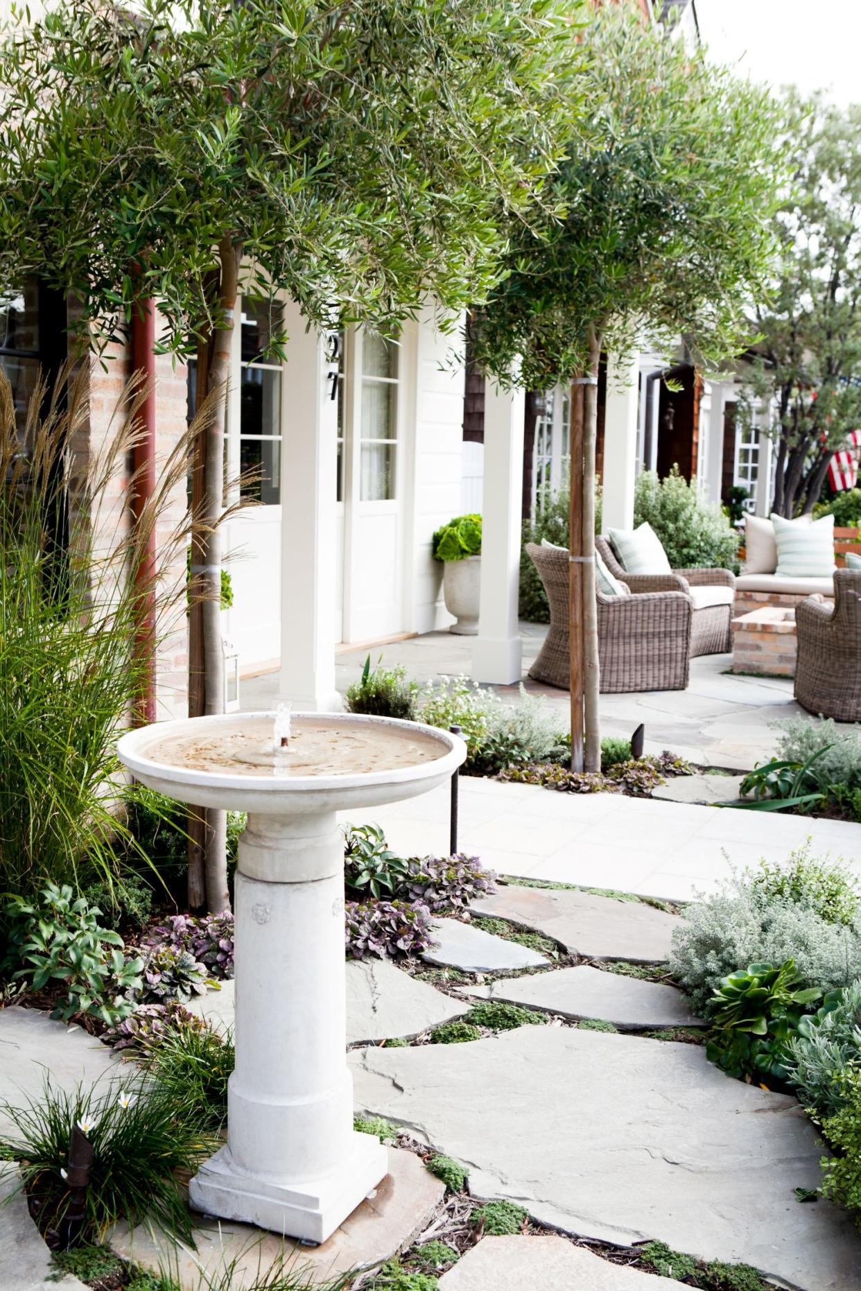  White house exterior with light stones edged with various low growing plants and a water feature. 