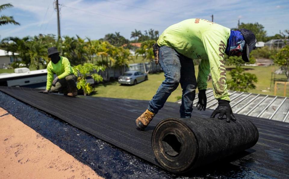 Jorge Tzunux, 30, right, and Danilo Mateo, 22, left, roll roofing felt over a layer of hot tar.
