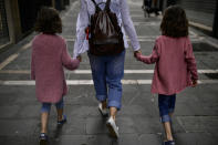 A family go for a walk taking their hands along a street of the old city, in Pamplona, northern Spain, Sunday, April 27, 2020. On Sunday, children under 14 years old will be allowed to take walks with a parent for up to one hour and within one kilometer from home, ending six weeks of compete seclusion. (AP Photo/Alvaro Barrientos)
