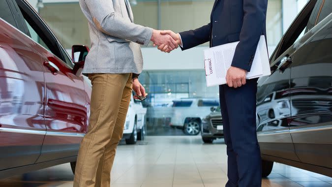 Low section side view of  handsome client shaking hands with sales manager in car showroom, after buying brand new luxury car.