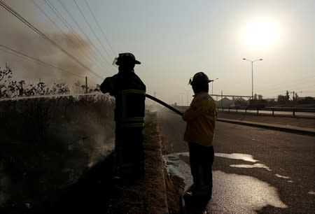 Firefighters spray water in a burning area at the outskirts of Santa Cruz