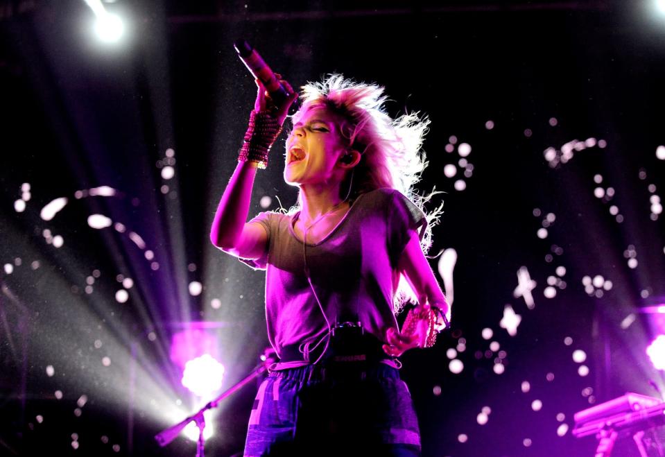 Grimes in purple-pink lighting singing into a microphone.