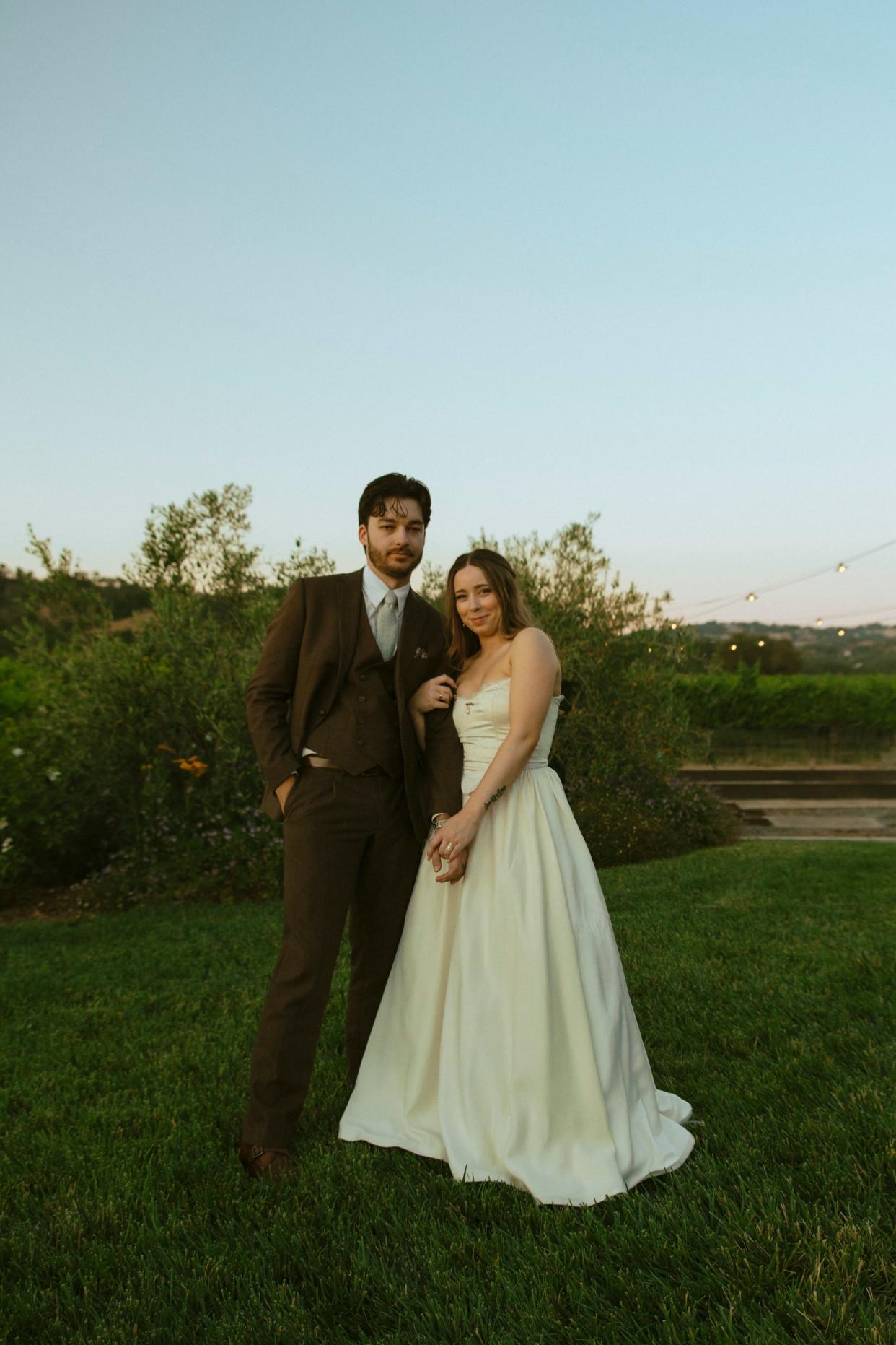 A bride and groom embrace in a field in their wedding attire.