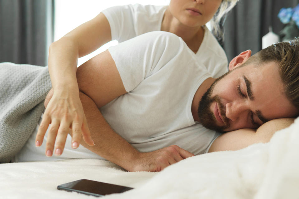 A woman reaches for her sleeping husband's phone