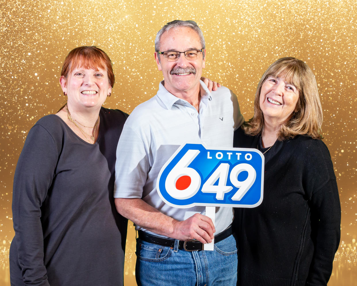 Three recent lottery winners standing with a Lotto 6/49 sign in front of a gold background.