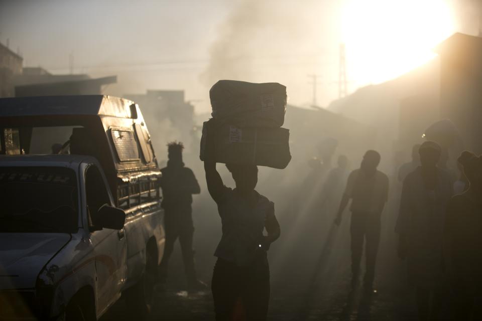 A vendor carries away her salvaged merchandise from the burned ruins of the Guerite Market that was engulfed in flames in Port-au-Prince, Haiti, early Tuesday, Jan. 14, 2020. (AP Photo/Dieu Nalio Chery)