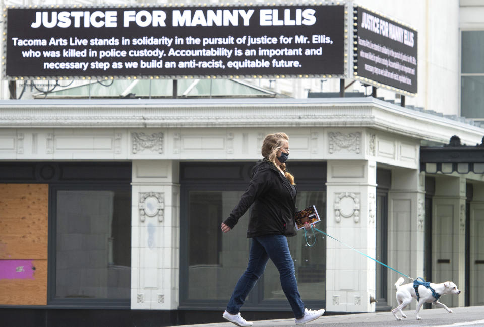 Monica Colby walks her dog, Piper, past the marquee on the historic Pantages Theater that honors Manny Ellis in downtown Tacoma, Washington, on Thursday, May 27, 2021. Earlier in the day, the state's attorney general announced criminal charges against three Tacoma police officers involved in Ellis' death. (Tony Overman/The News Tribune via AP)