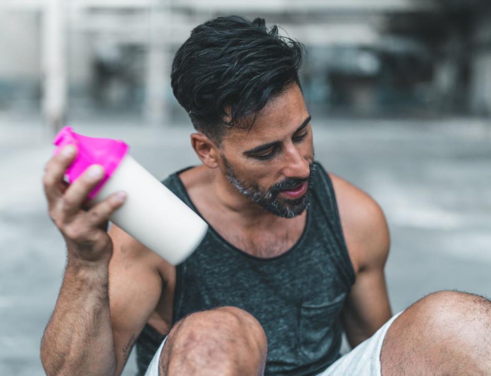 a man is sitting down to mix a protein shake after en exercise inside an abandoned warehouse