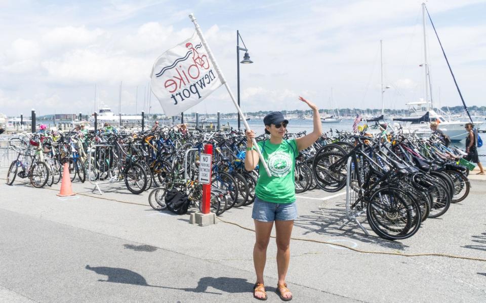 Bike Newport volunteer Kandace Matzker holds a flag while welcoming bicyclists to Fort Adams State Park for the Newport Folk Festival in 2017.