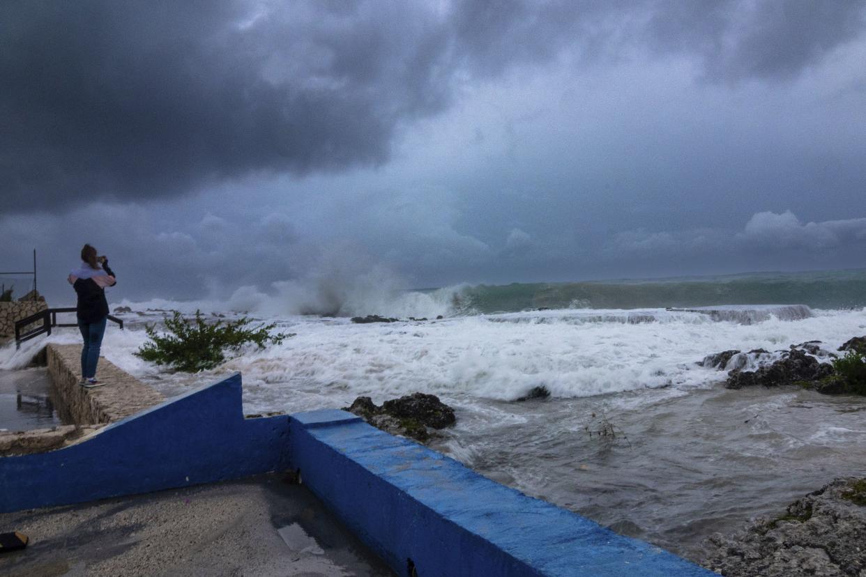 A woman takes photos while waves crash against a seawall as Hurricane Ian passes through George Town, Grand Cayman island, Monday, Sept. 26, 2022.
