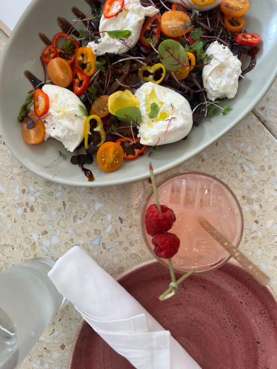 a plate of colorful salad next to a pink cocktail