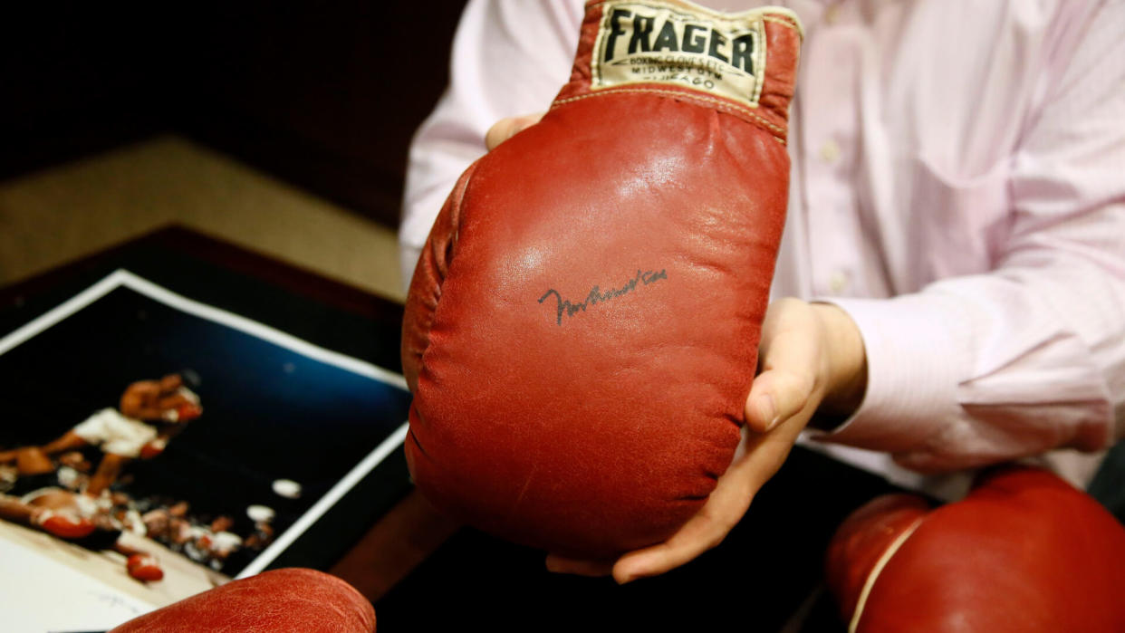 Mandatory Credit: Photo by Tony Gutierrez/AP/Shutterstock (6103227e)Sonny Liston, Muhammad Ali Heritage Auctions Director of Sports Auctions, Chris Ivy, holds the autographed glove of Muhammad Ali with the gloves of Sonny Liston sitting on the table below at the auction house, in Dallas.