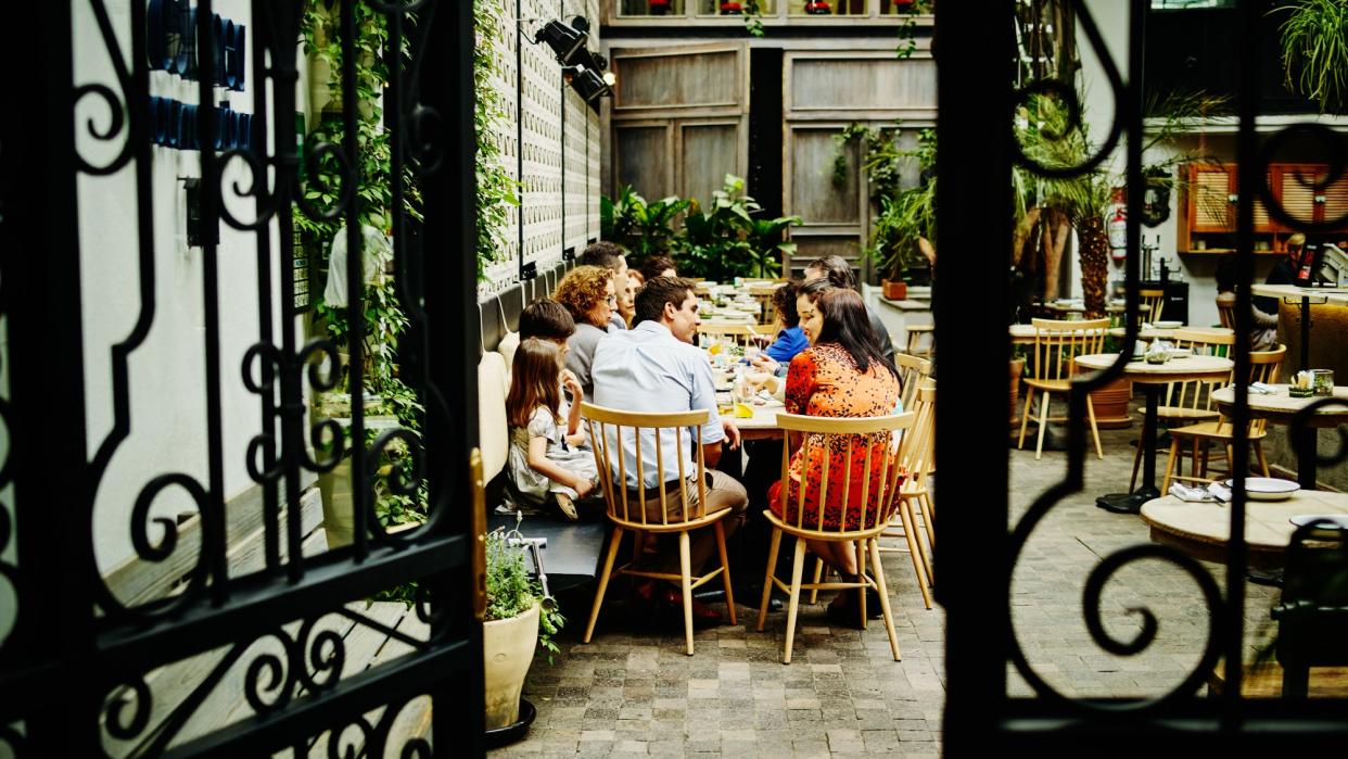  View through the gate of a multi-generational family dining at an outdoor restaurant. 