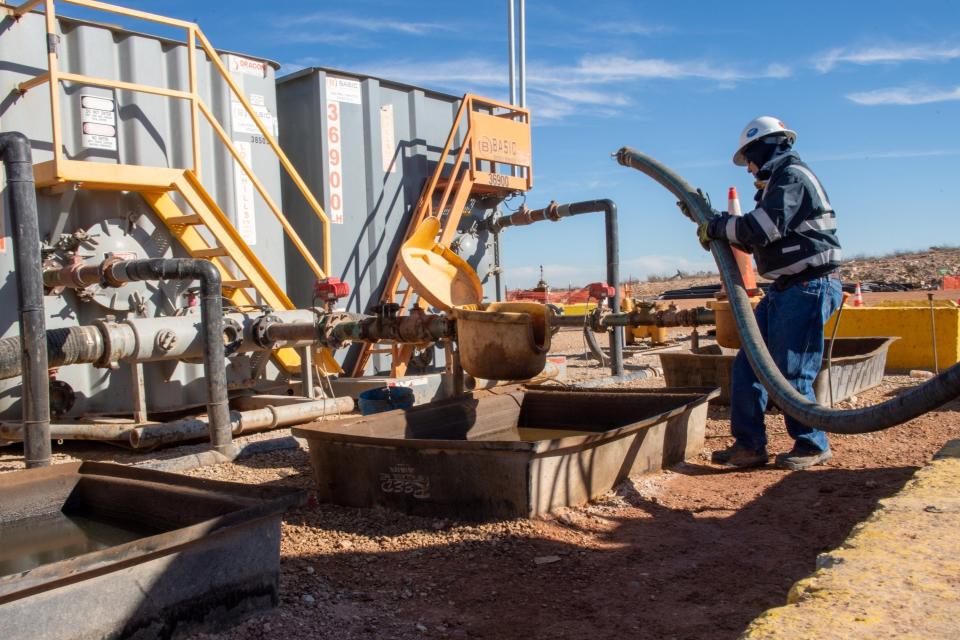 An oil worker hooks up a hose from a tanker truck to pump produced water from a fracking well into a treatment facility, near Malaga, New Mexico.